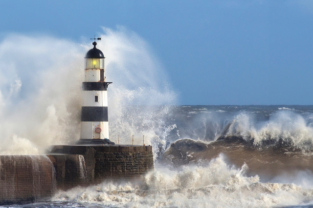 Lighthouse being struck by powerful ocean waves during a storm, symbolizing resilience, guidance, and maritime strength.